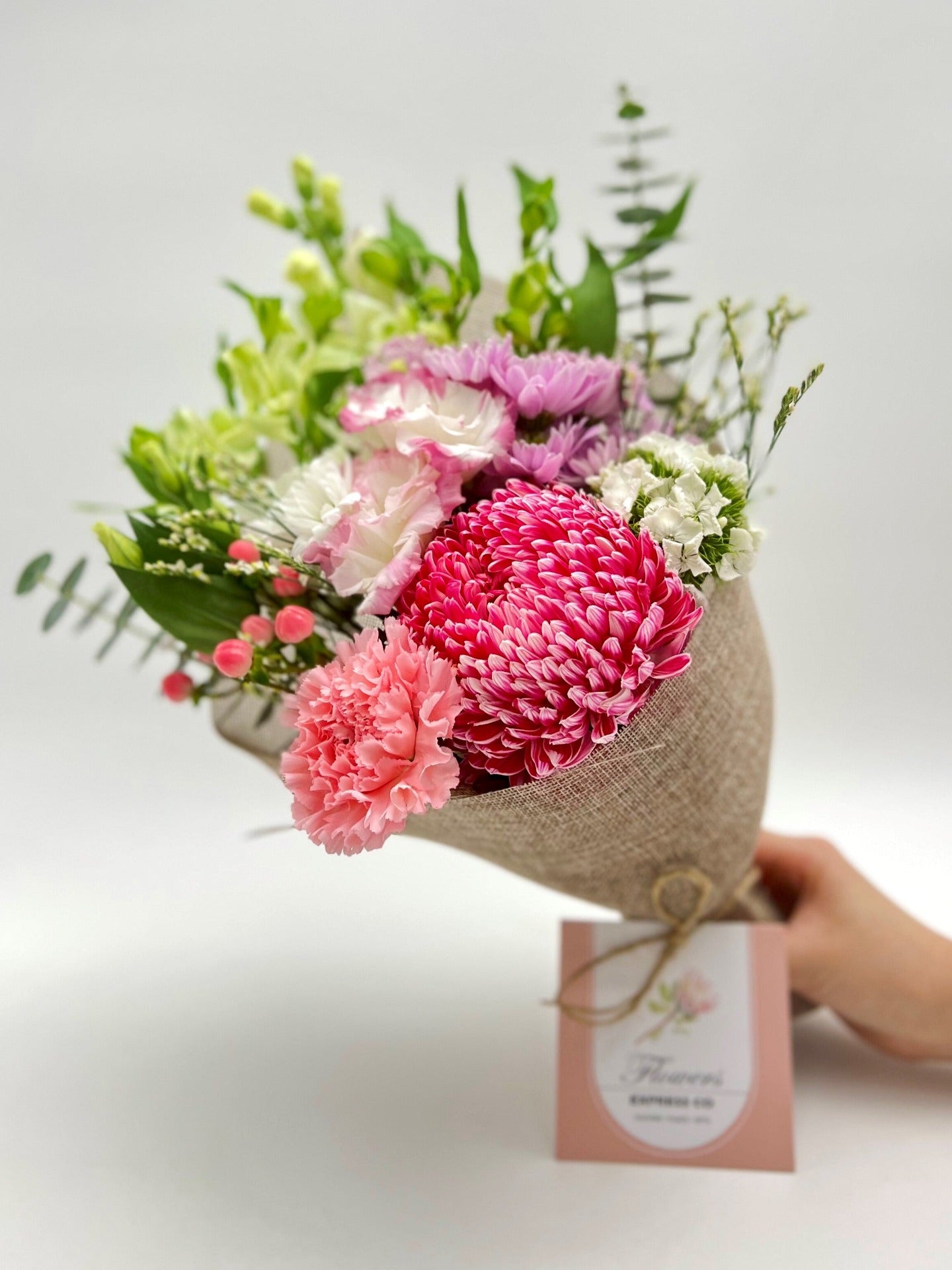 A handmade bouquet of pink disbuds mum, carnations, and other pink or white flowers handcrafted in Melbourne held by a florist from Flowers Express Co. 