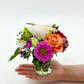 A bouquet of colourful flowers in a vase lies in a person's hand. Available in Melbourne.