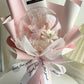 A pink and white decorative flower bouquet with a clear round bubble containing dried flowers, wrapped in pink tissue paper and ribbon with printed text.