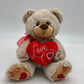 A photo of a charming light brown teddy bear. The teddy bear is adorned with a red ribbon around its neck and holds a red heart with the word “Love” written in white cursive letters.