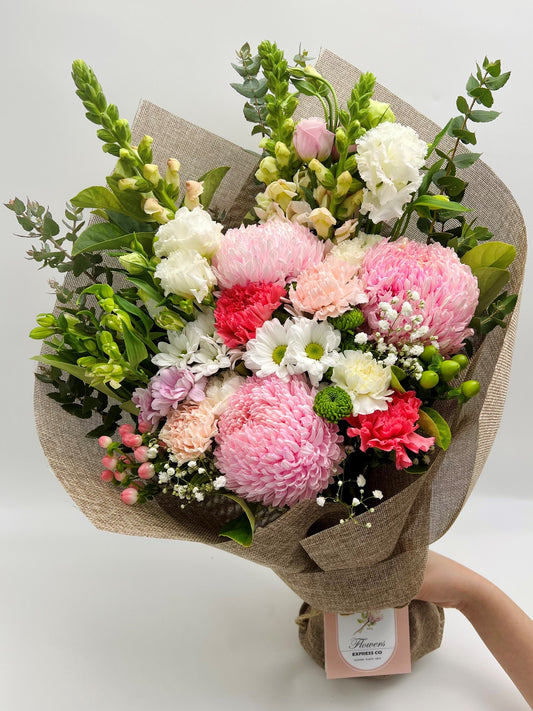 A pink bouquet of disbuds mum flowers is held in hand against a white background and made in Melbourne by a florist at Flowers Express Co.