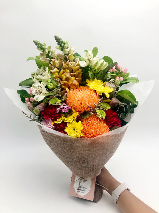 A vibrant bouquet with mixed blooms and lush greens, wrapped in hessian. Shot by Flowers Express Co in Melbourne.