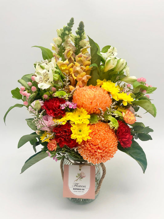 A vibrant bouquet of orange and red flowers in a glass jar, tied with twine and a Flowers Express Co tag, shot in Melbourne.