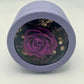 A photo of a stunning dark purple rose, beautifully preserved and displayed in a light purple round gift box. It’s a timeless symbol of elegance and beauty.