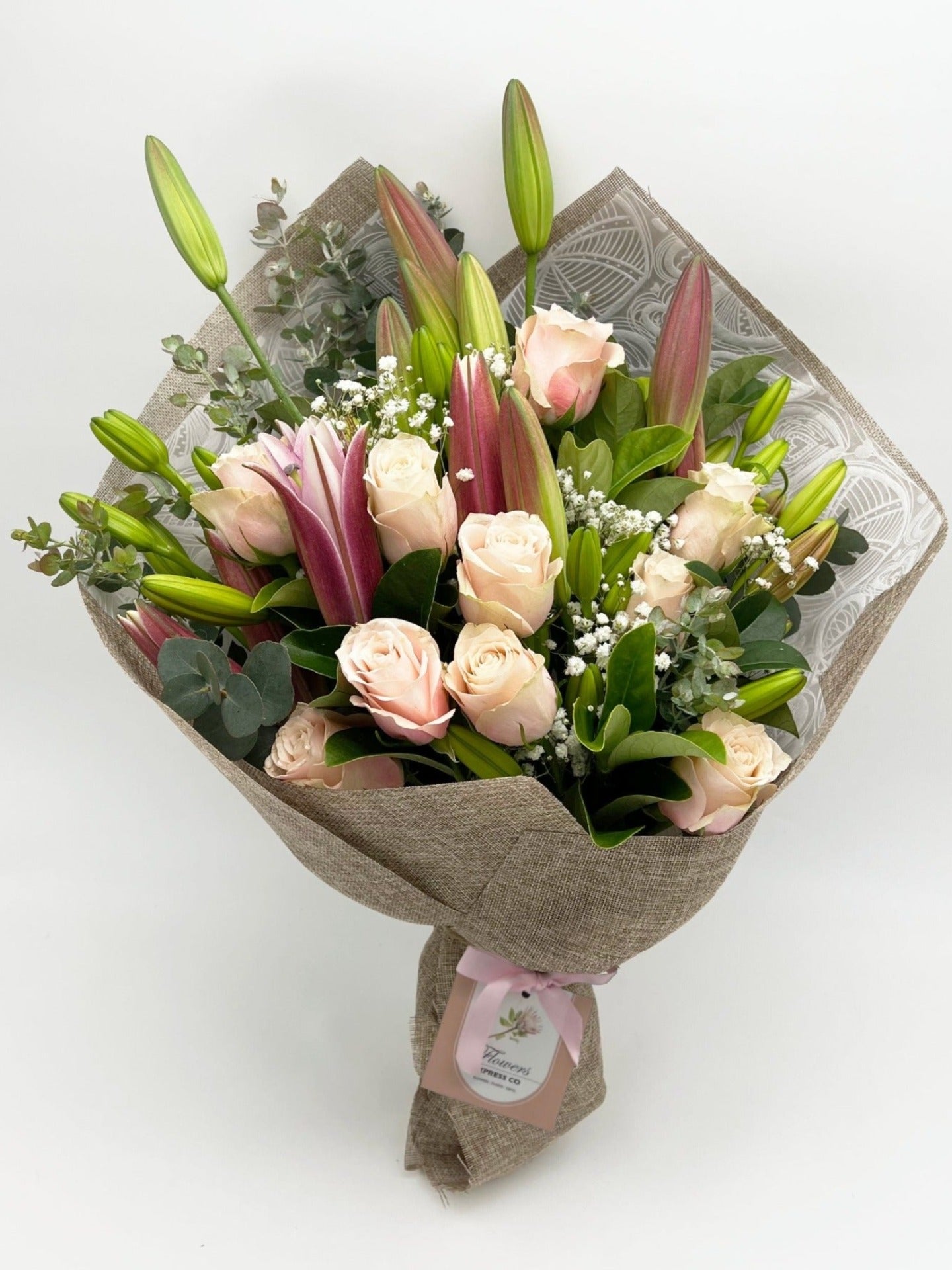 A bouquet of lilies and pink roses, crafted by a Melbourne florist from Flowers Express Co, elegantly wrapped in jute against a pristine white wall backdrop.