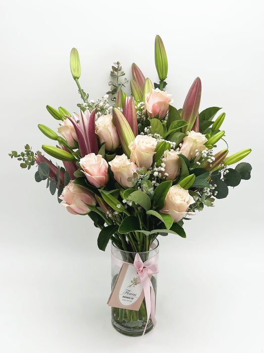 A bouquet of pink roses and lilies, handcrafted in Melbourne by a florist, in a glass vase and decorated with a pink ribbon.