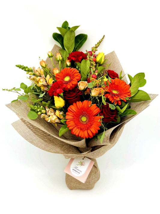 Vibrant orange and red bouquet with gerberas, roses, and lush green foliage