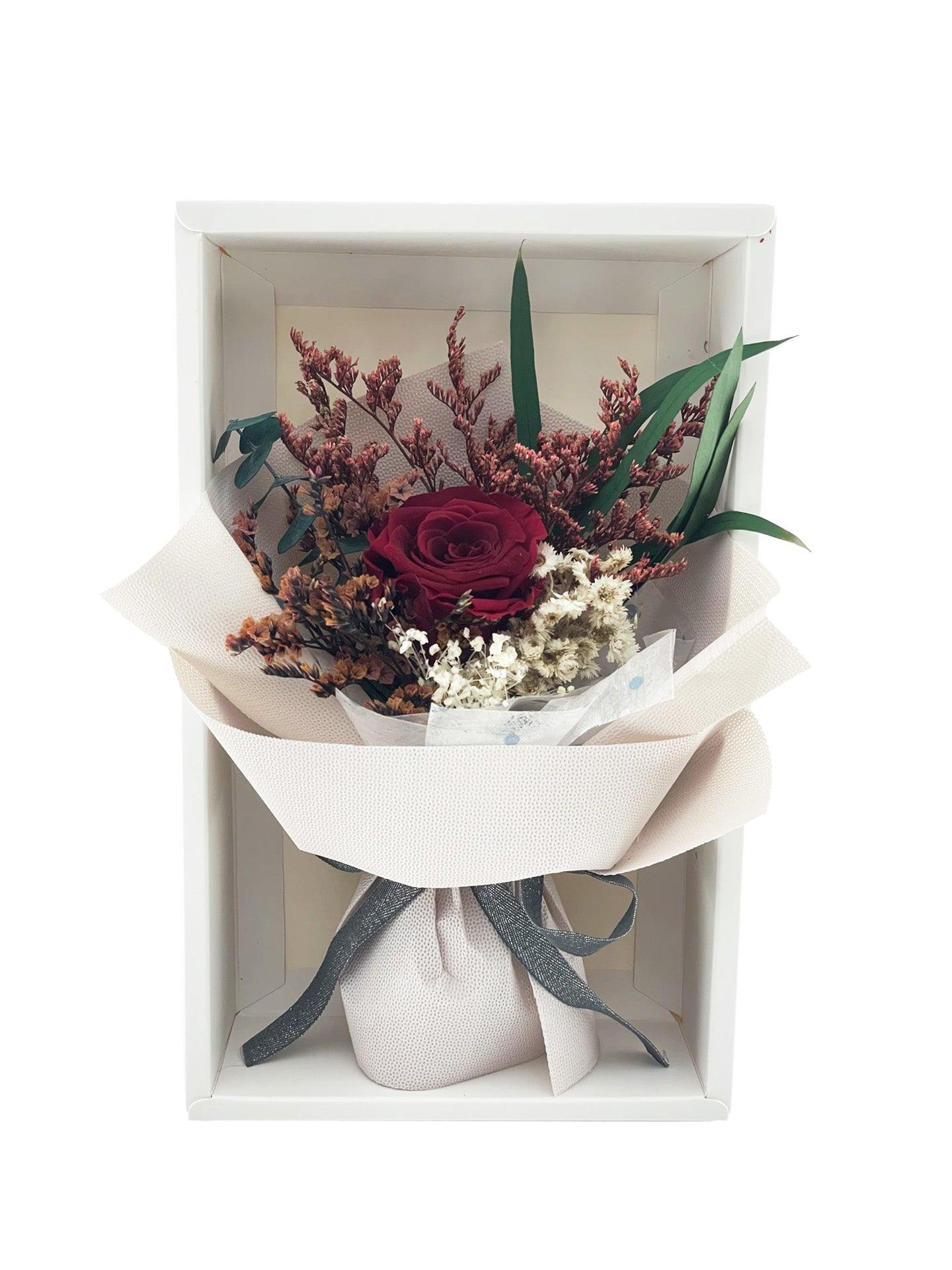 Red preserved rose and dried flowers in beige wrapping paper with grey ribbon, elegantly arranged in a white box.