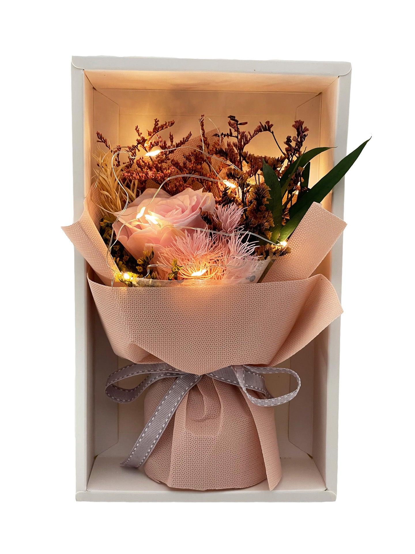 A white box containing a pink preserved rose and assorted dried flowers with fairy light encased in the delicate yellow wrap and adorned with a grey ribbon, made by Flower Express Co florists in Melbourne.